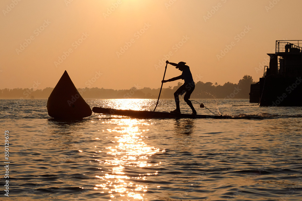SUP silhouette of teenager standing with a paddle on the surfboard at sunset. Stand up paddle boarding competitions on the calm river