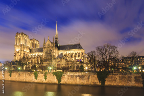 Beautiful cityscape view of the Notre-Dame Cathedral and river Seine in Paris, France, on a rainy spring evening at night