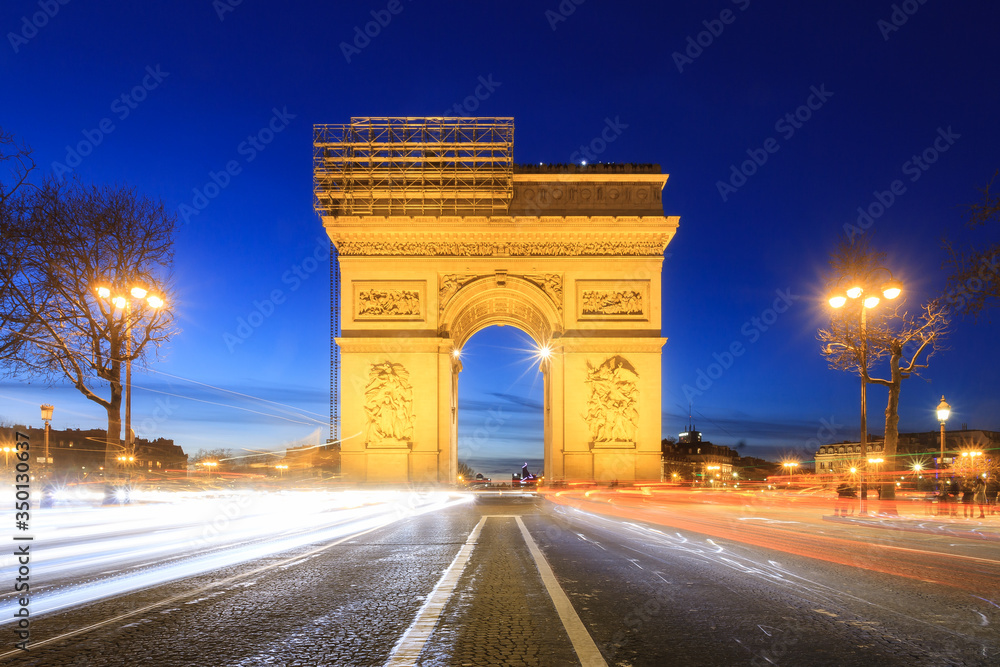 Beautiful cityscape urban street view of the Arc de Triomphe in Paris, France, on a spring evening after sunset in the blue hour, seen from the Champs-Elysees with traffic