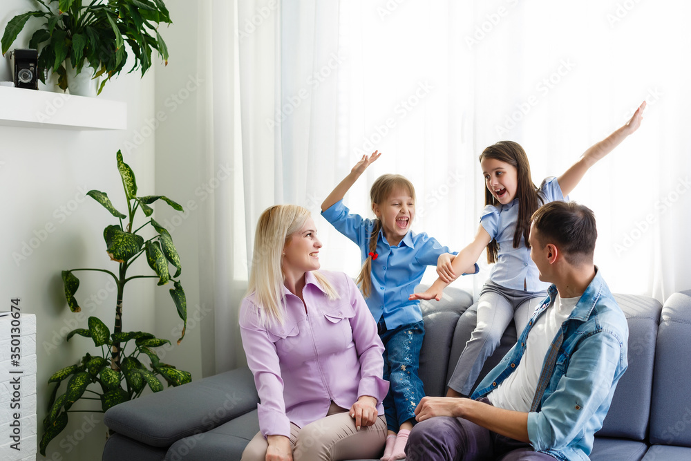 Cheerful young family with kids laughing sitting on couch together, parents with children enjoying entertaining at home Cheerful young family with kids laughing sitting on couch together, parents with children enjoying entertaining at home