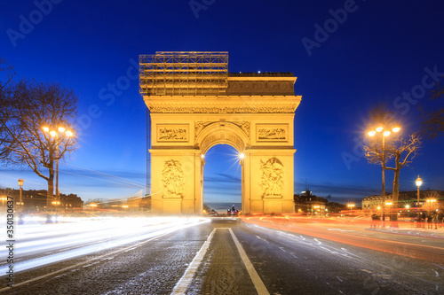 Beautiful cityscape urban street view of the Arc de Triomphe in Paris, France, on a spring evening after sunset in the blue hour, seen from the Champs-Elysees with traffic © dennisvdwater