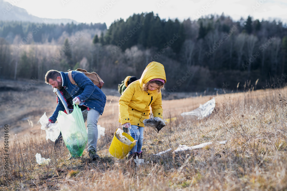 Small child with activists picking up litter in nature, environmental pollution concept. Small child with activists picking up litter in nature, environmental pollution concept.
