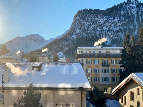 Sankt Moritz (Schweiz) Berglandschaft mit Schnee im Winter bei Blauem Himmel in den Alpen mit Sicht auf ein kleines Dorf, mit Schnee bedeckten Dächern und einer Kirche und Alpen mit einer Papeterie  photo