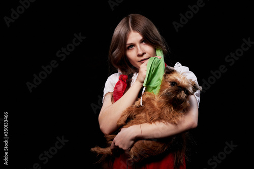 Girl in protective medical green mask and national ethnic dress holding small dog in her hands. Coronavirus, COVID-19 pandemic concept. Domestic animal allergy, sneezing and coughing near of pets