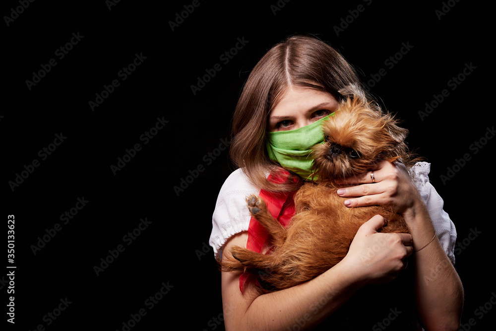Girl in protective medical green mask and national ethnic dress holding small dog in her hands. Coronavirus, COVID-19 pandemic concept. Domestic animal allergy, sneezing and coughing near of pets