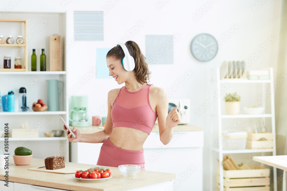 Waist up portrait of smiling young woman dancing in kitchen and listening to music while preparing fitness lunch, copy space Waist up portrait of smiling young woman dancing in kitchen and listening to music while preparing fitness lunch, copy space