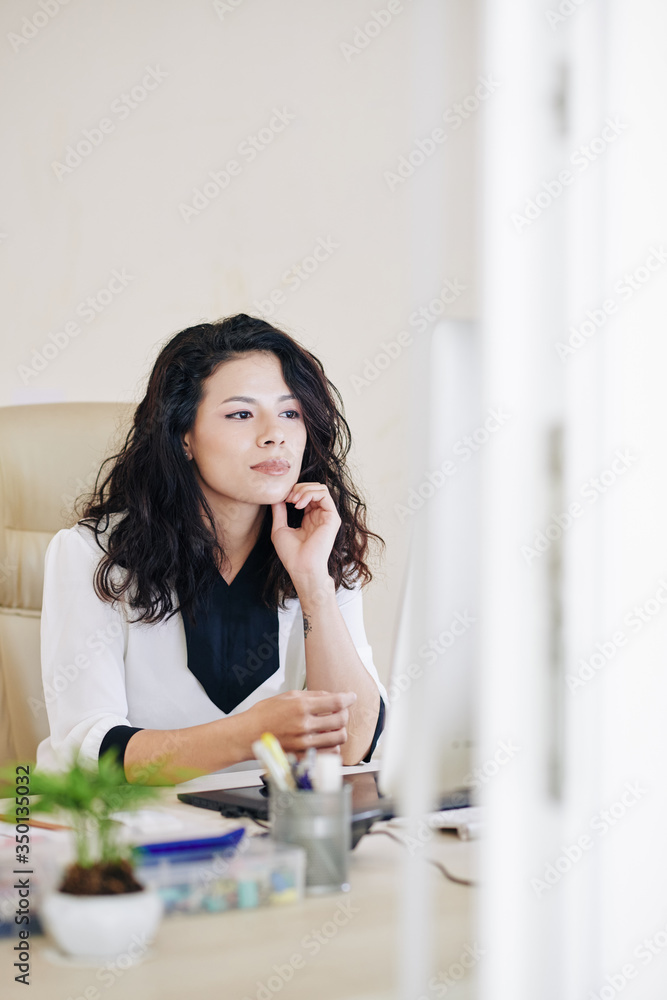 Pensive young mixed-race businesswoman reading article on computer screen Pensive young mixed-race businesswoman reading article on computer screen