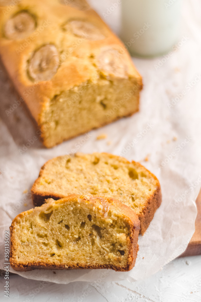 Homemade sliced healthy banana bread ready for serve on breakfast on the white concrete background with craft baking paper and pastry knife. Top view. Close up shoot