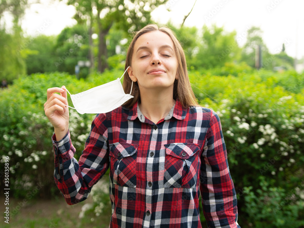 Happy young girl takes off a medical mask and breathes fresh air in nature. Rejoices over the end of the coronavirus pandemic and isolation. Happy young girl takes off a medical mask and breathes fresh air in nature. Rejoices over the end of the coronavirus pandemic and isolation.