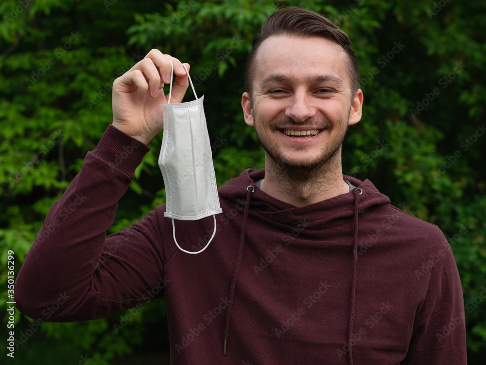 Happy young guy takes off his medical mask and breathes fresh air in nature. Rejoices over the end of the coronavirus pandemic and isolation. Happy young guy takes off his medical mask and breathes fresh air in nature. Rejoices over the end of the coronavirus pandemic and isolation.