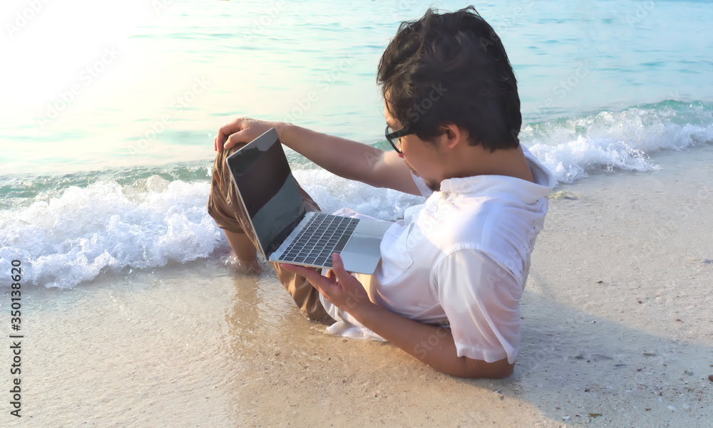 Relaxed young man with laptop sitting on the sandy beach with soft waves. Internet of things concept.