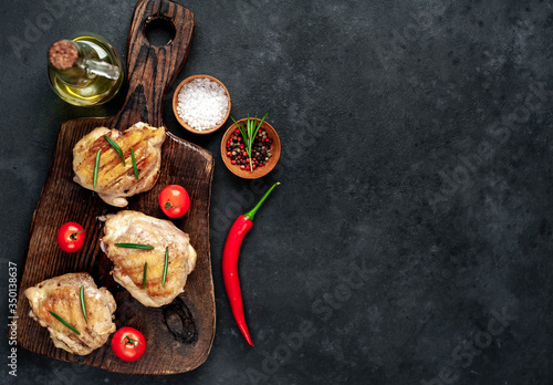 Skinless grilled chicken thighs with spices on a cutting board on a stone background with copy space for your text