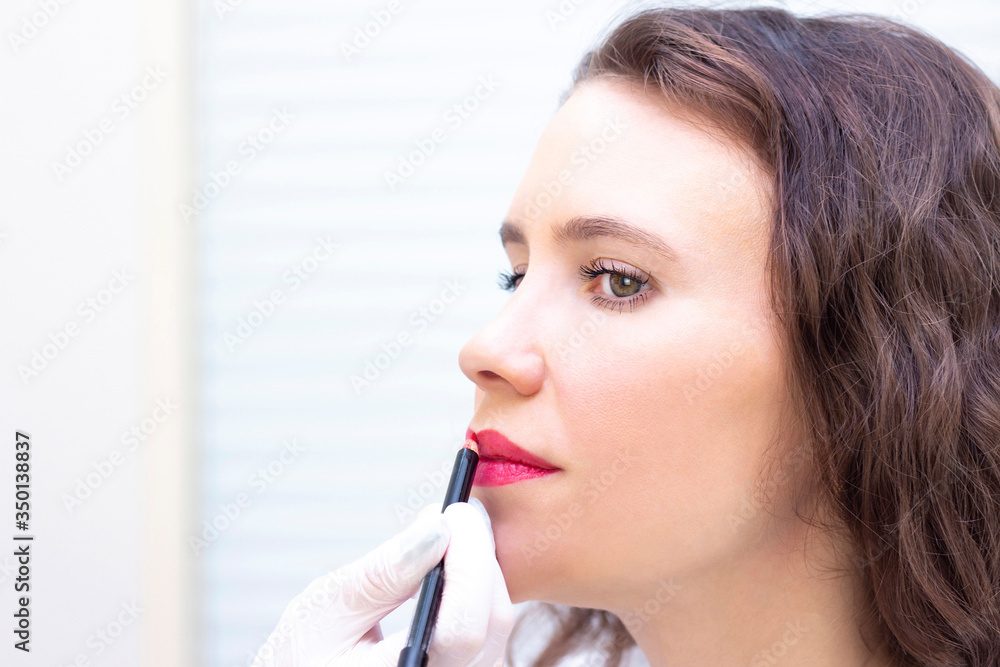 Young woman having permanent makeup on her lips at the beauticians salon. Permanent Makeup (Tattoo). drawing a contour with a white lip pencil Young woman having permanent makeup on her lips at the beauticians salon. Permanent Makeup (Tattoo). drawing a contour with a white lip pencil
