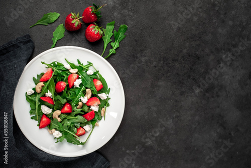 Salad of arugula, nuts, strawberries, cheese in a white plate on a stone background with copy space for your text. Healthy food.