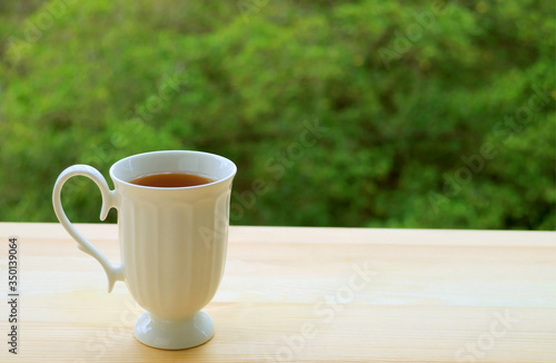 One cup of hot tea isolated on outdoor table with blurry green foliage in background 