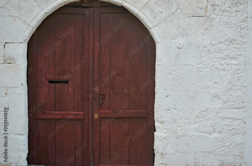 a semicircular, wooden, brown door surrounded by whitewashed walls of a village house. greek style architecture