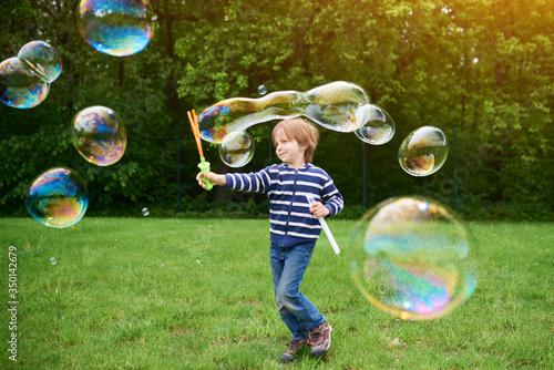 Valokuva Outdoors portrait of cute preschool boy blowing soap bubbles on a green lawn at the playground