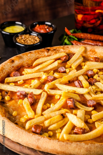 Italian Cuisine. Thin Oktoberfest pizza with french fries, hunting sausages and corn. Background image. copy space