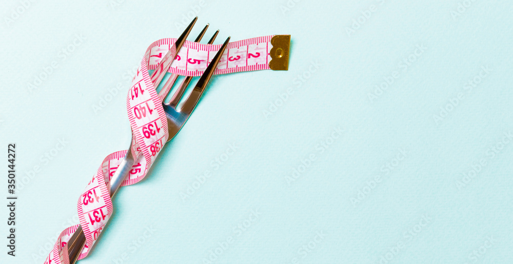 Obraz premium Fork wrapped in measuring tape on blue background. Top view of overeating concept