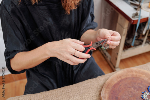 Close-up image of woman using pliers to attach french hook to earring she made