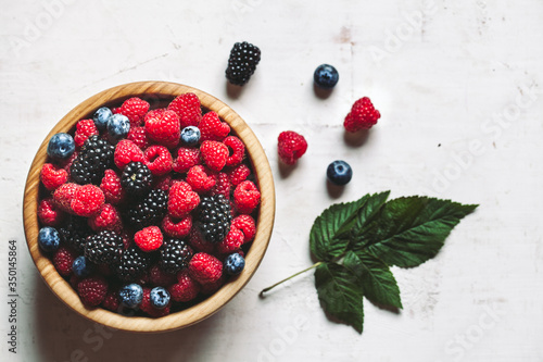 Juicy fresh blueberries, raspberries and blackberries in a white plate on old wooden background