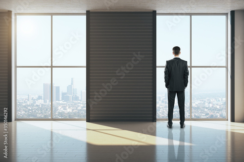 Businessman standing in clean gallery interior with city view.