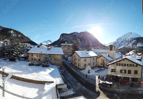  Sankt Moritz (Schweiz) Berglandschaft mit Schnee im Winter bei Blauem Himmel in den Alpen mit Sicht auf ein kleines Dorf, mit Schnee bedeckten Dächern und einer Kirche und Alpen mit Hotels und Straße © MariaLuisa