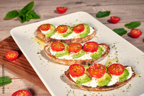 Healthy food, tomato and avocado toasts on a wooden cutting table.
