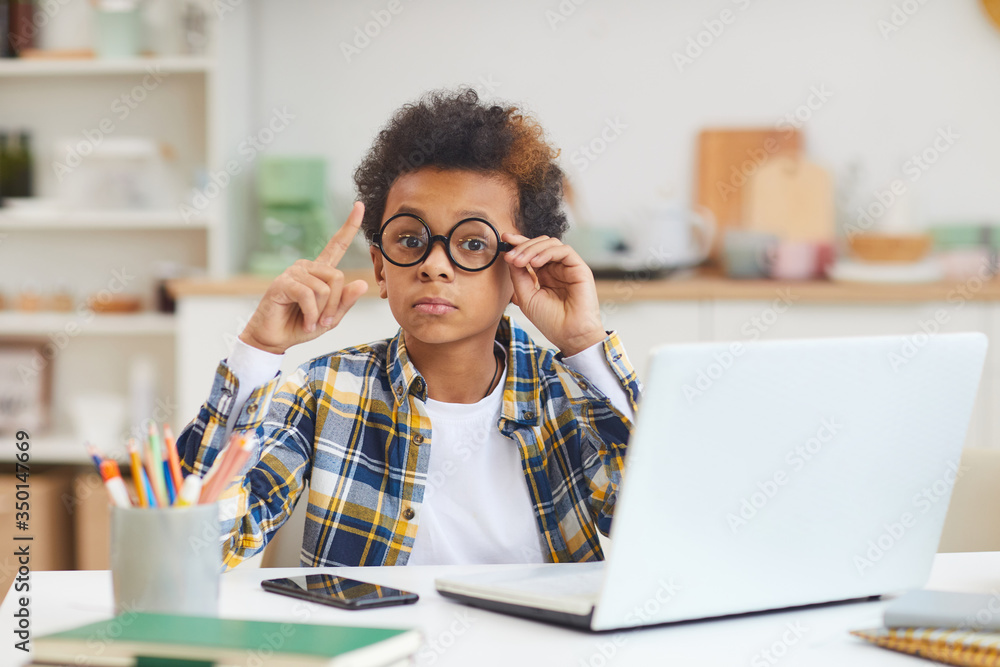 Portrait of cute African boy using laptop and wearing big glasses while studying at home, remote education concept, copy space Portrait of cute African boy using laptop and wearing big glasses while studying at home, remote education concept, copy space