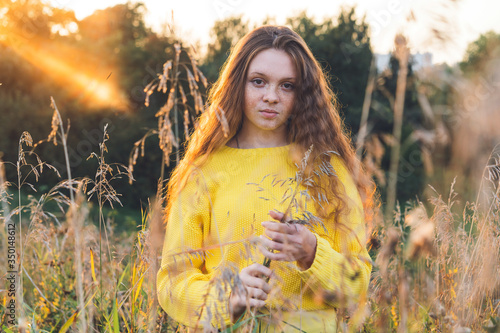 Cheerful smiling teenage girl of 14 years old with long curly red hair in a yellow sweater on the nature. Summer vacation weekend concept. Selective focus 