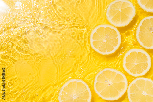 Slice of lemon underwater or in water with splashing and droplet top view flat lay on yellow background