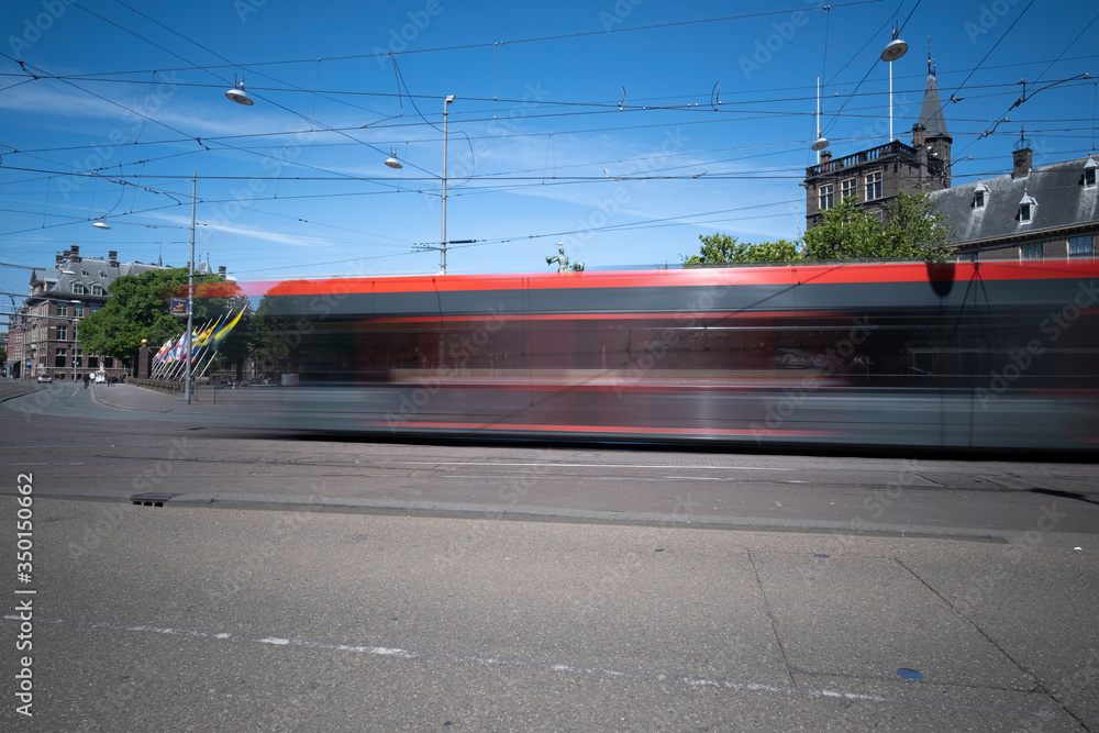 A moving tram at day, houses in background, blue sky, in long exposure. The Hague, the Netherlands