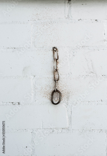 Part of an old chain on a background of a white brick wall.