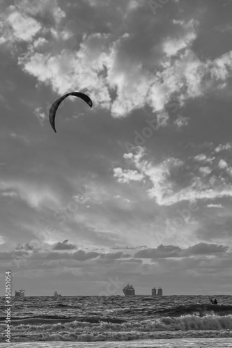 Extreme Sport Kitesurfing, cargo ships on the horizon. Surfer in the sea at Scheveningen at sunset. Black and white