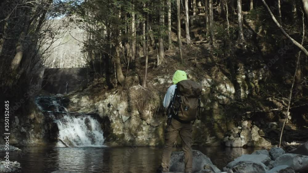 A waterfall and a waterfall pot flowing down in a virgin forest with thick grass and trees, and a traveler who sees it. A waterfall and a waterfall pot flowing down in a virgin forest with thick grass and trees, and a traveler who sees it.