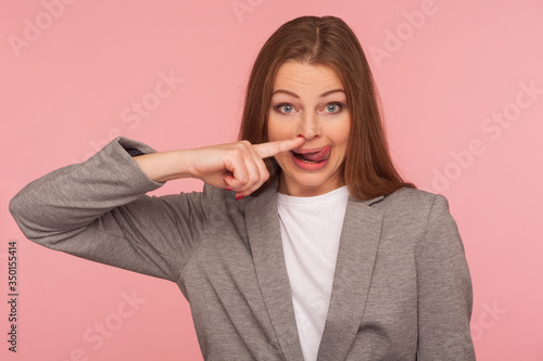 Photos Portrait of funny young woman in business suit picking her nose, showing tongue out, removing boogers with comical wondered expression, bad habit