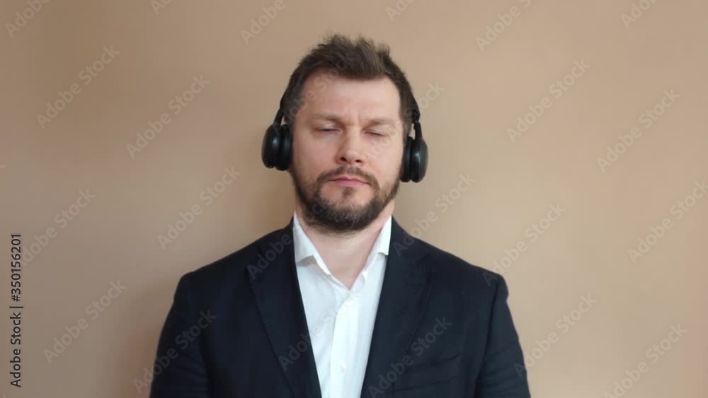 Young man in a suit and white shirt listens to music with headphones on a beige background. Businessman communicates via video, uses his smartphone. Modern communications. Video call. Young man in a suit and white shirt listens to music with headphones on a beige background. Businessman communicates via video, uses his smartphone. Modern communications. Video call.