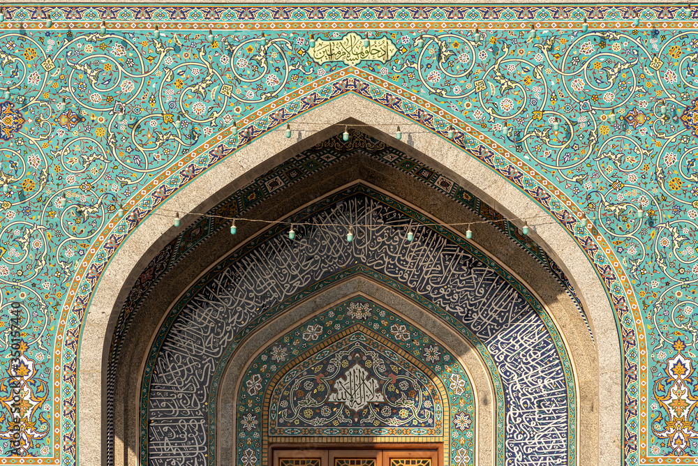 Exterior of mosque facade with white columns and amazing ornamental tiles decorating wall, Iran.