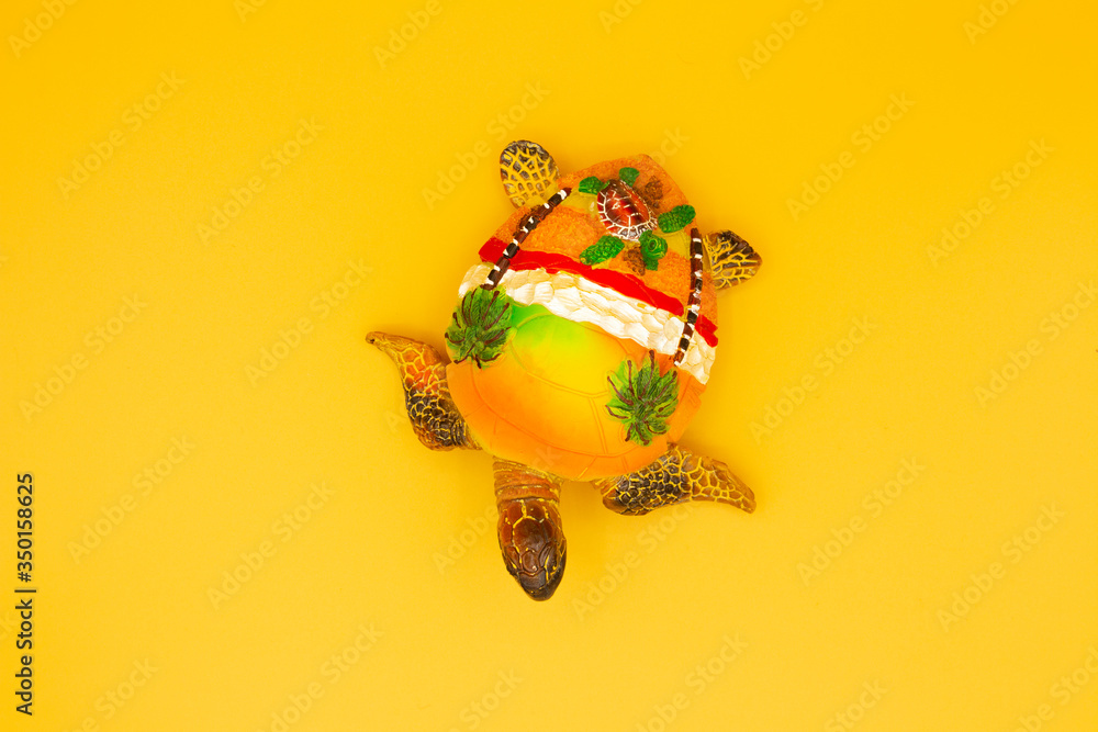 Souvenir yellow turtle on a yellow background. The view from the top. On the shell are palm trees, the sea and a turtle.