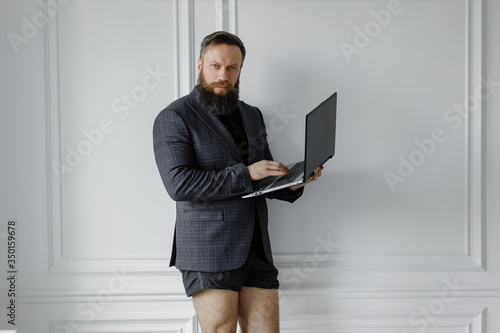 A bearded man in a jacket and without pants works at home in isolation.