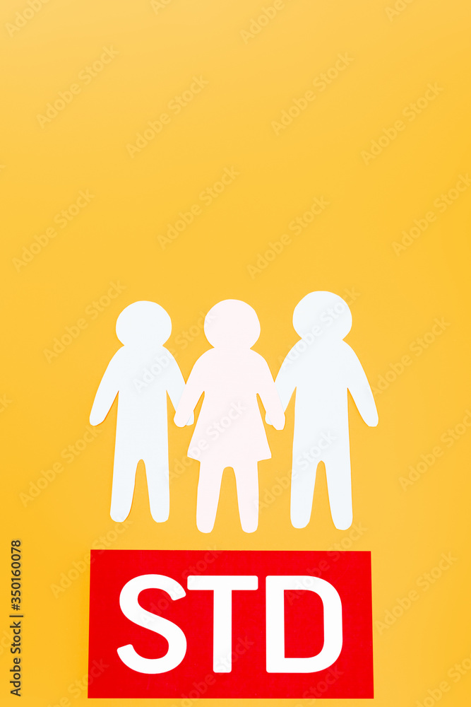 top view of three paper people near red paper with std lettering isolated on orange top view of three paper people near red paper with std lettering isolated on orange