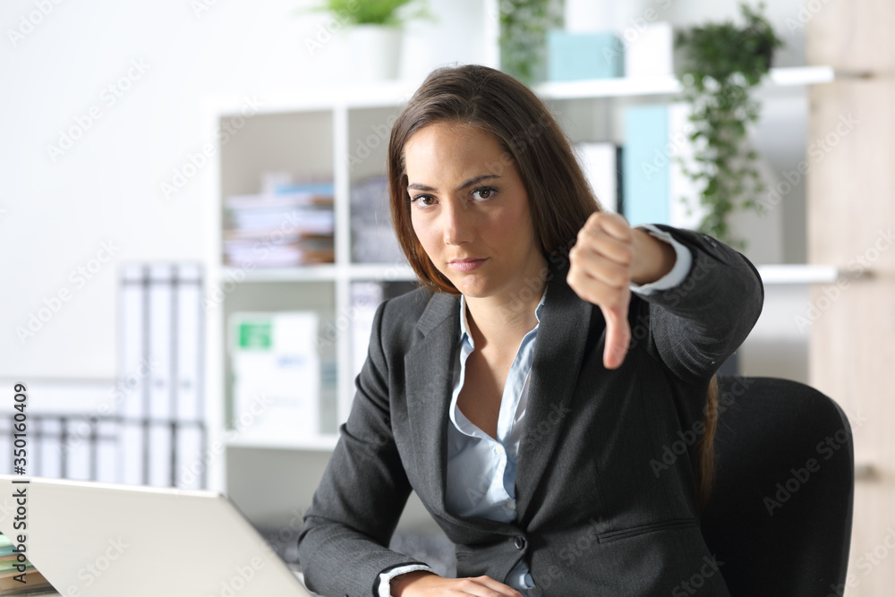 Serious executive gesturing thumbs down at office Serious executive gesturing thumbs down at office