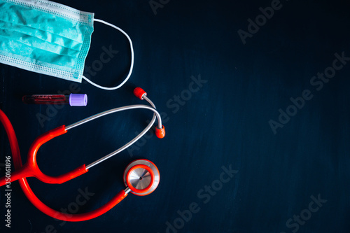 Red stethoscope and white surgical medical mask on black board, black edit space for your text. Black Edit space. Coronavirus protection concept photo