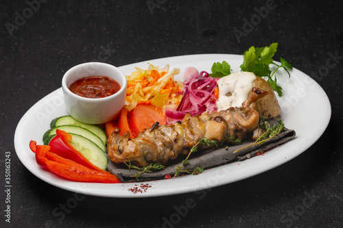 Meat skewers on a plate with vegetables, traditional meat food on fire