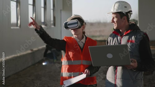 modern technologies, female and male engineer in viar glasses and laptop in hand in protective helmets discuss new building with help of additional reality on construction site photo