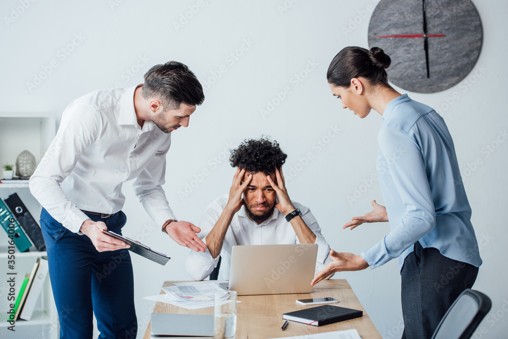 Obraz premium Multicultural business people looking at upset african american businessman at table in office
