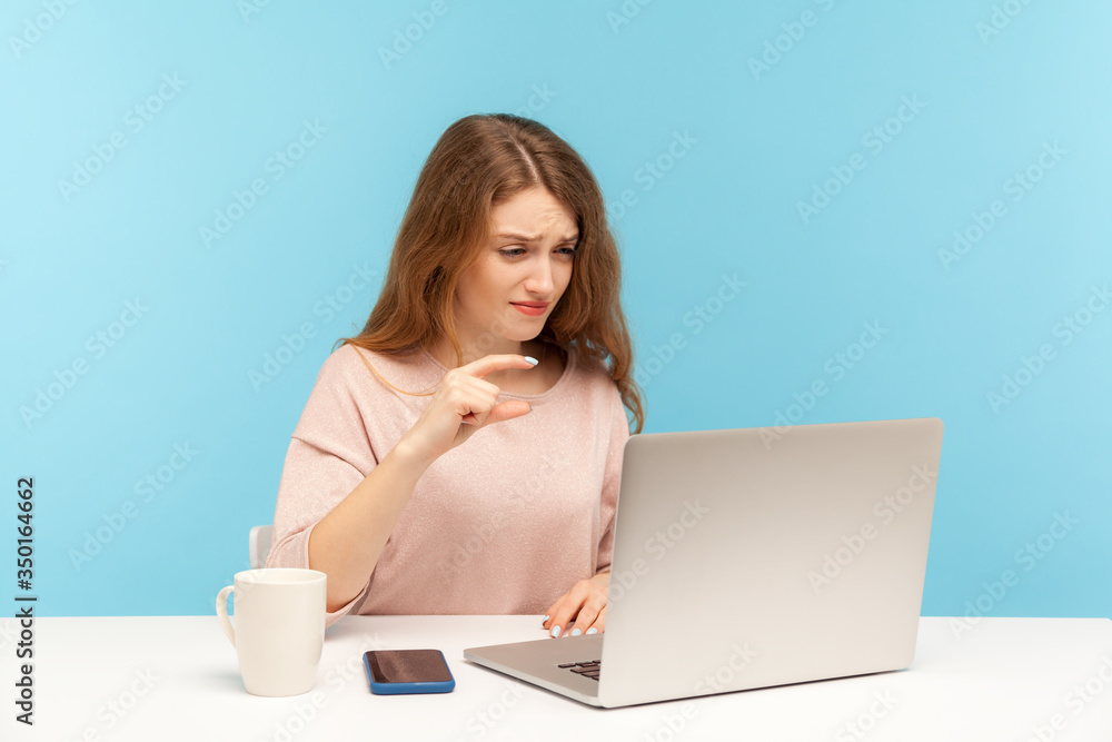 Small amount, low rating. Disappointed woman employee showing a little bit gesture to laptop screen, talking on video call, measuring minimum scale. indoor studio shot isolated on blue background Small amount, low rating. Disappointed woman employee showing a little bit gesture to laptop screen, talking on video call, measuring minimum scale. indoor studio shot isolated on blue background