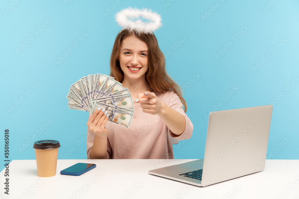 Φωτογραφία You deserve big money! Lovely angelic woman with nimbus sitting at laptop, holding dollar banknotes and pointing to camera, encouraging to earn wealth