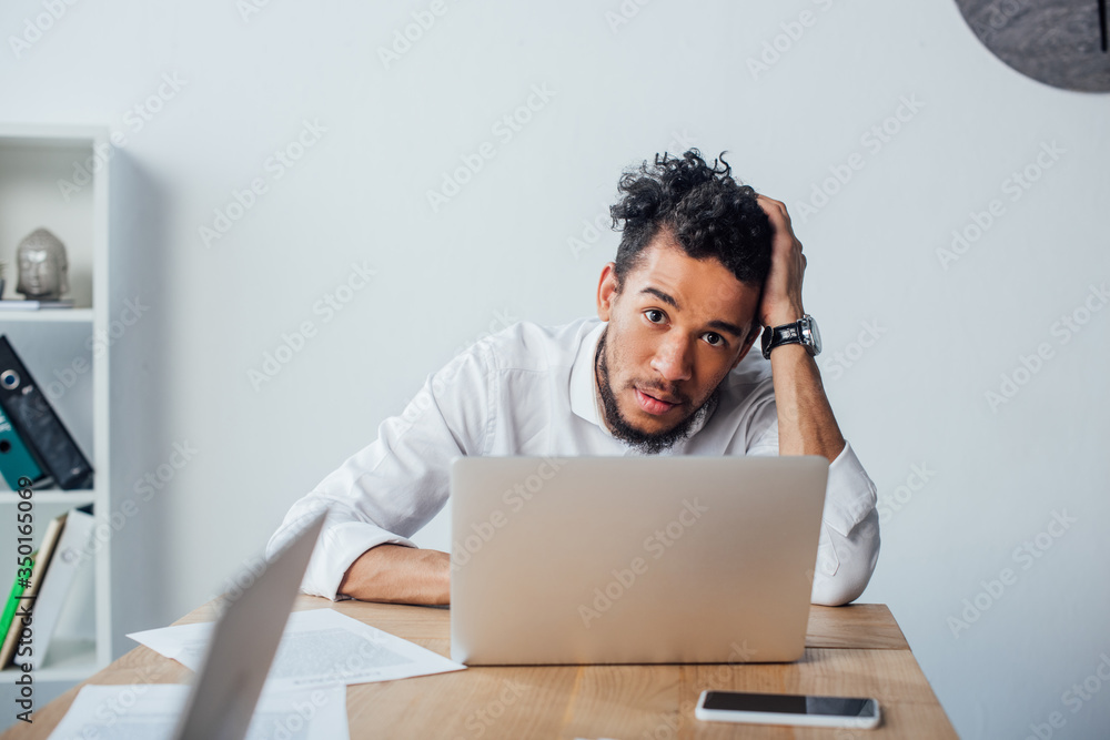 Selective focus of african american businessman looking at camera while working in office Selective focus of african american businessman looking at camera while working in office
