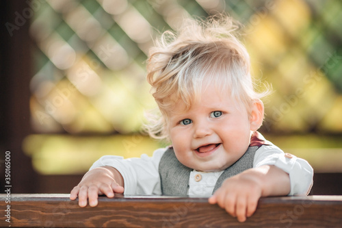 A pretty boy 1 year old smiling with long blond hair on a Sunny summer
